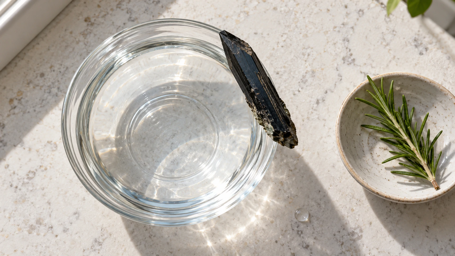 Dark blade-shaped aegirine stone at the edge of a glass bowl of water with rosemary